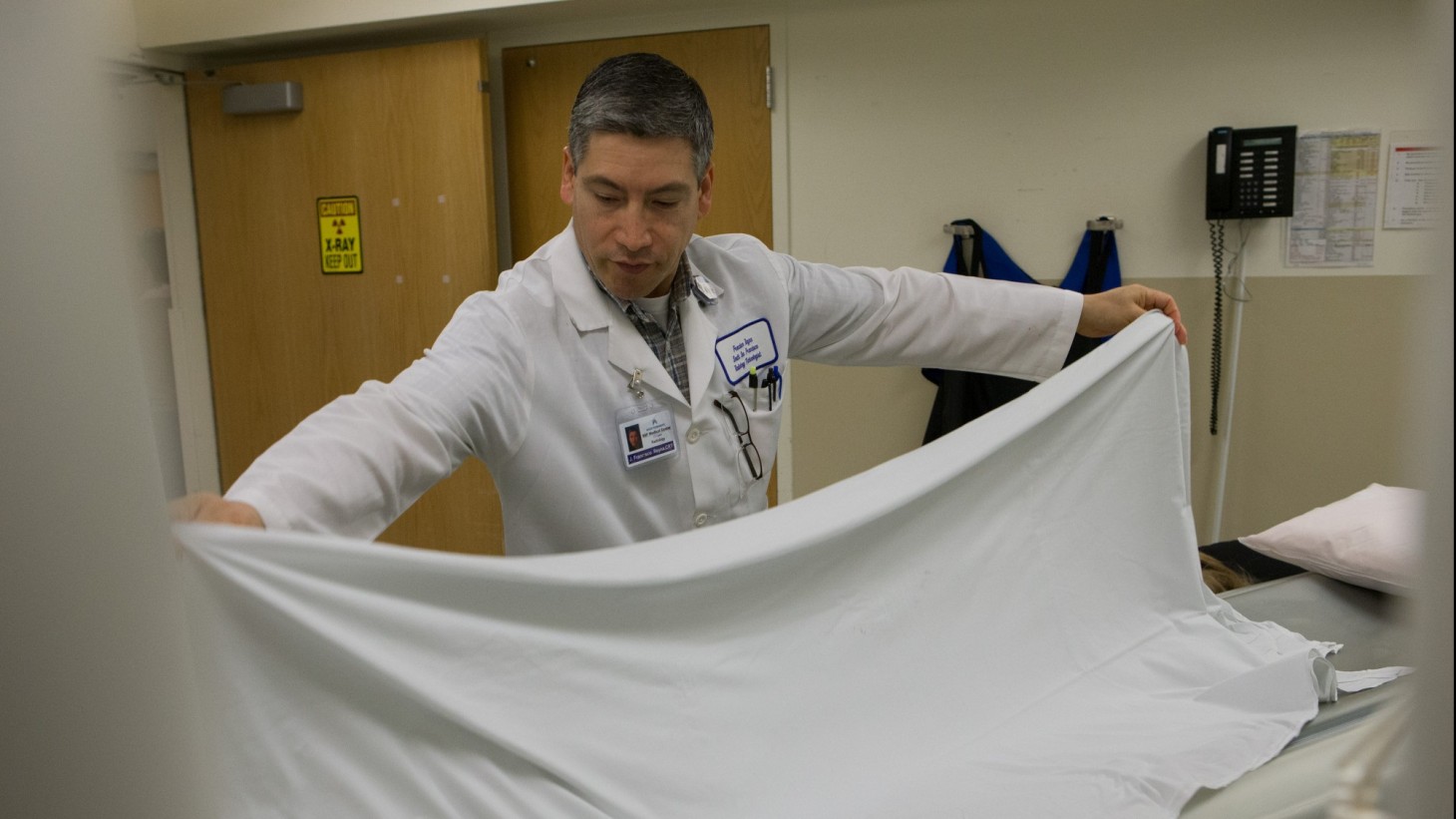 Health care worker putting a white sheet on a hospital bed