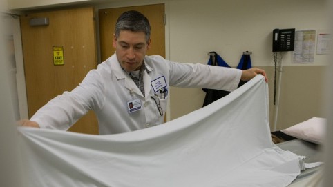 Health care worker putting a white sheet on a hospital bed