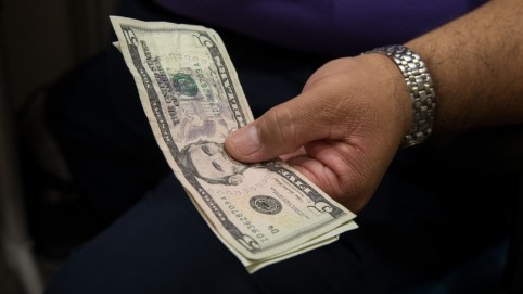 A man's hand holding a five dollar bill