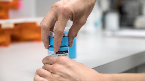 A pair of hands opening a blue medication bottle