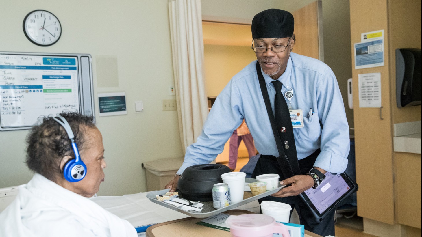 Food service worker bringing a patient her meal in her hospital room.