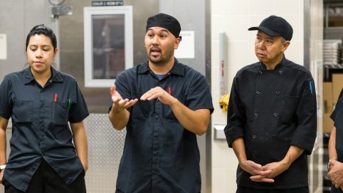 3 kitchen workers dressed in black discussing a serious issue