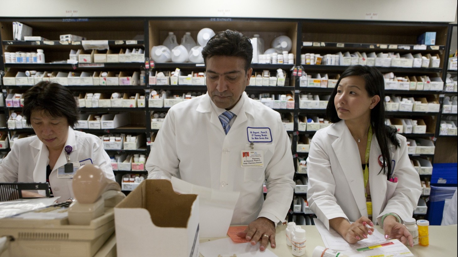 Three pharmacy workers working in front of a wall of medications